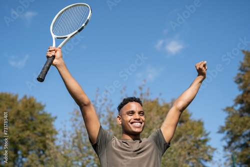 Smiling man raising arms with tennis racket