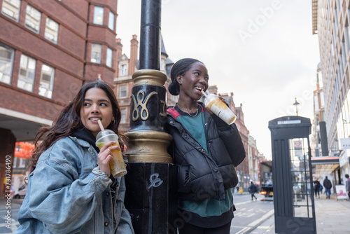 Two cheerful women drinking bubble tea while leaning against lantern