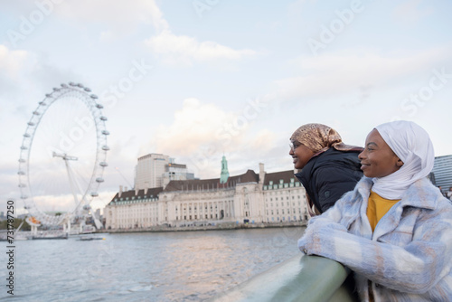 UK, London, Female tourists in hijabs looking at London Eye over River Thames © Cultura Creative