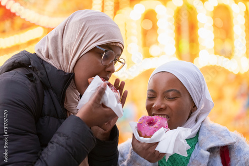 Young female tourists in hijabs eating donuts photo