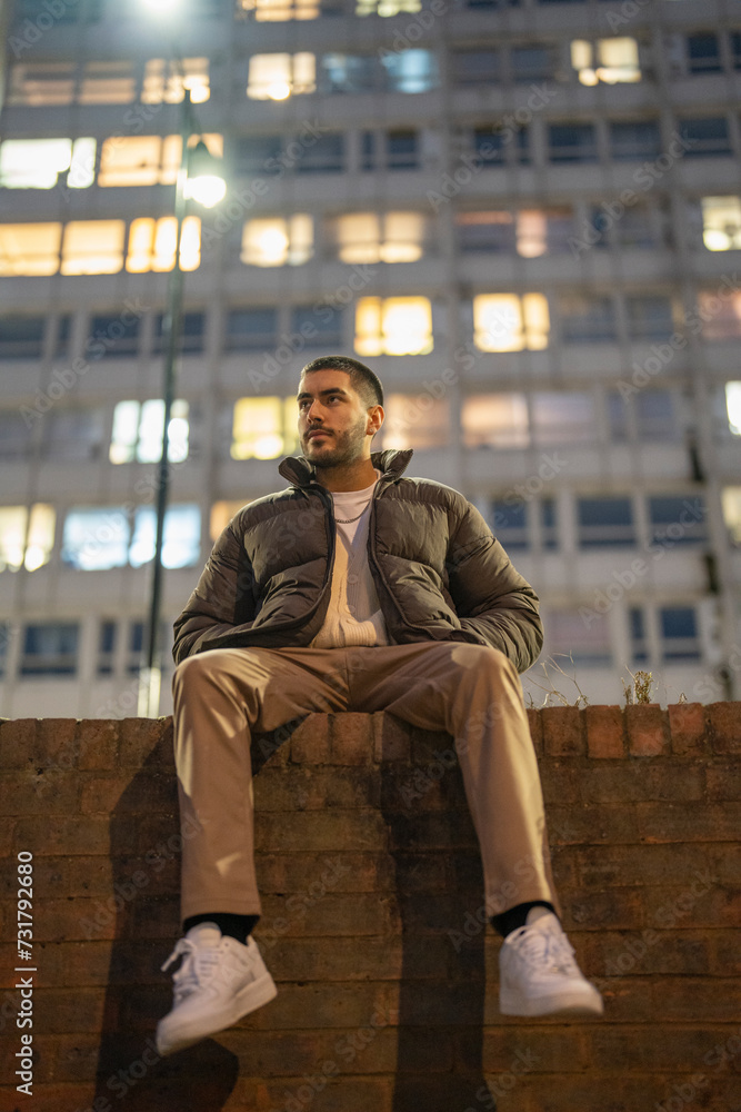 Obraz premium Young man sitting on brick wall at night