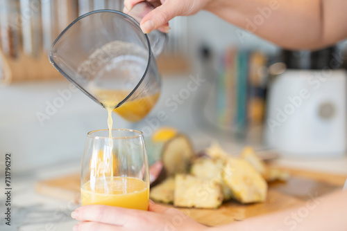 Woman in kitchen, pouring freshly made smoothie, close up