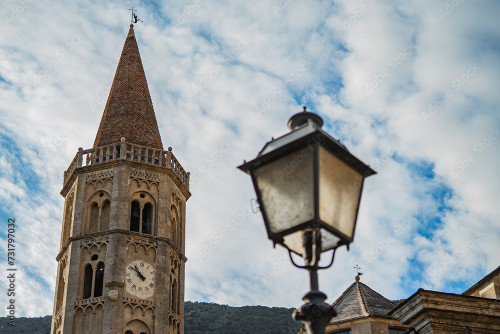 A close up shot of a village of Finalborgo, Finale Ligure, a medieval street lantern(out of focus) with an old church(in focus) on the background and a beautifull cloudy sky, sunset time, Italy 