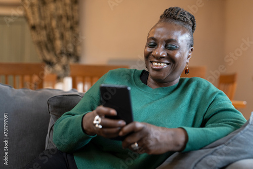 Smiling senior woman relaxing on sofa and using phone