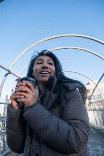 Portrait of smiling woman in jacket holding disposable cup on footbridge