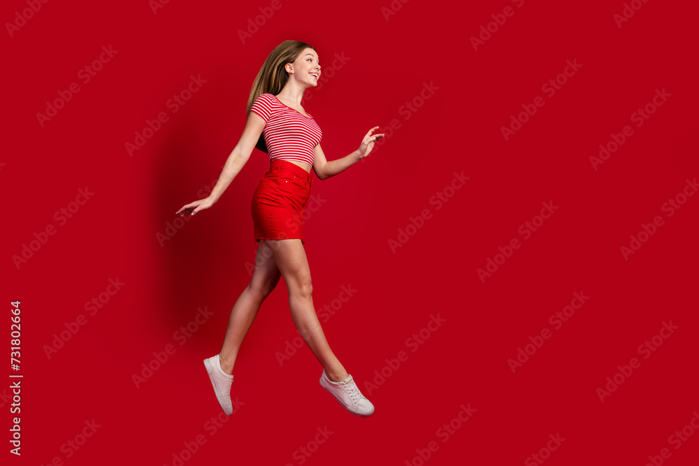 Full length photo of cool pretty lady dressed striped top mini skirt jumping high walking empty space isolated red color background