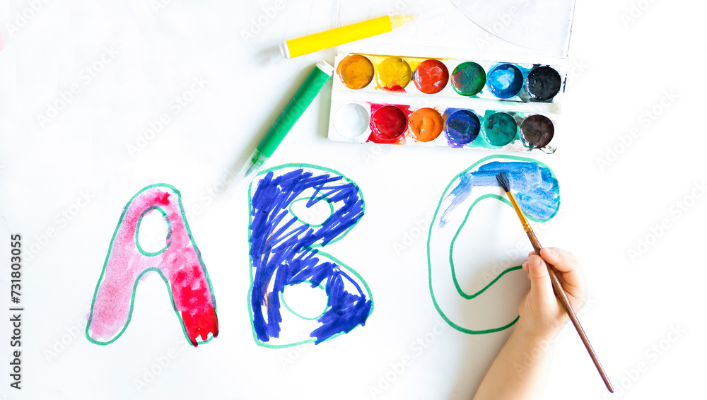 Letters of the ABC alphabet, inks, markers drawn on a white sheet of paper. A banner for school, a close-up of a child's hand, a child coloring letters on a school poster. Photo with copy space Letters of the ABC alphabet, inks, markers drawn on a white sheet of paper. A banner for school, a close-up of a child's hand, a child coloring letters on a school poster. Photo with copy space