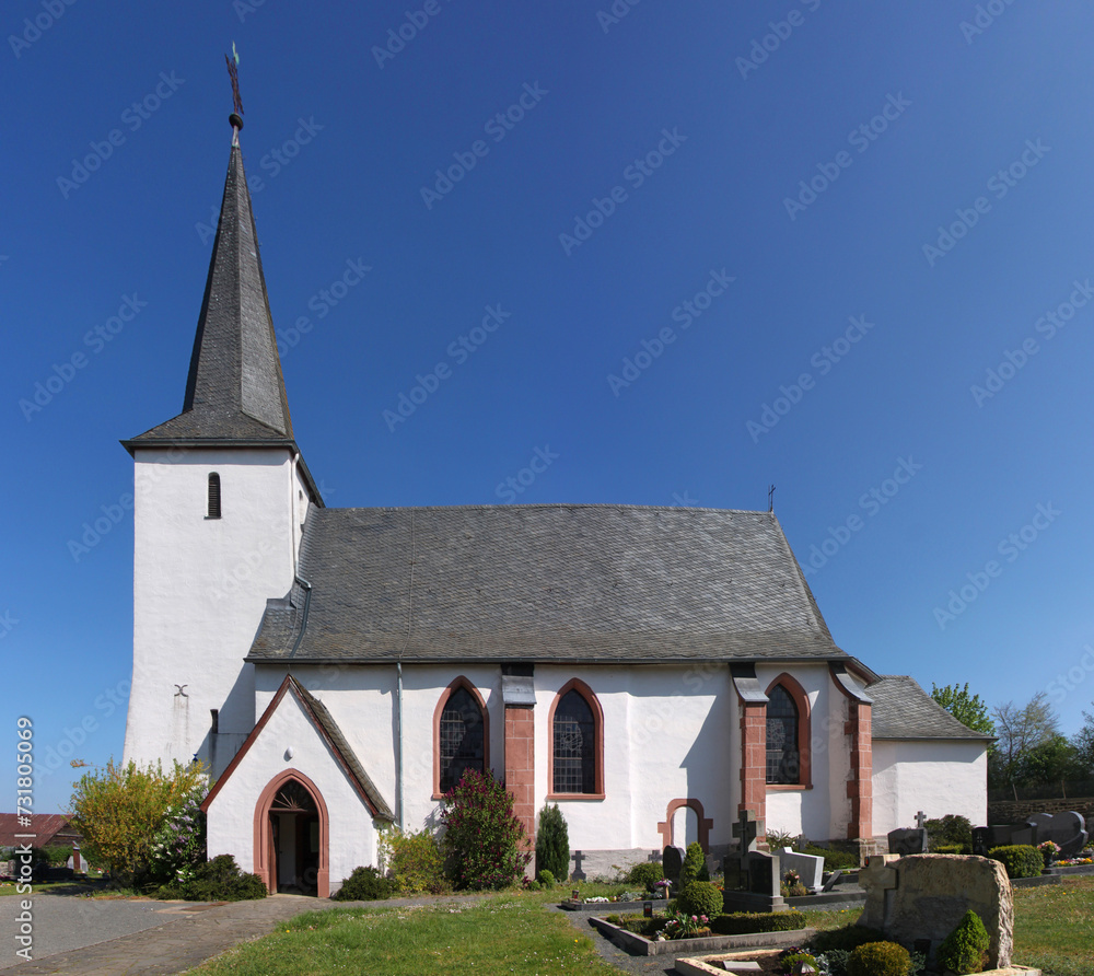 Gothic St. Willibrord church with white bell tower and cemetery in Elcherath village, Eifel region in Germany