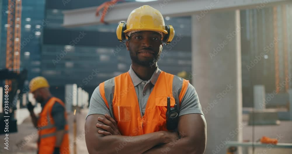Happy Professional Heavy Industry Engineer Wearing Safety Uniform and Hard Hat on a Residential Building Construction Site. Smiling African American Industrial Site Manager Standing Outdoors Happy Professional Heavy Industry Engineer Wearing Safety Uniform and Hard Hat on a Residential Building Construction Site. Smiling African American Industrial Site Manager Standing Outdoors