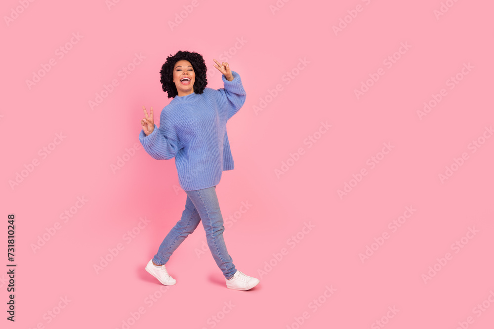 Full body photo of attractive young woman walk show v-sign wear trendy blue knitted clothes isolated on pink color background