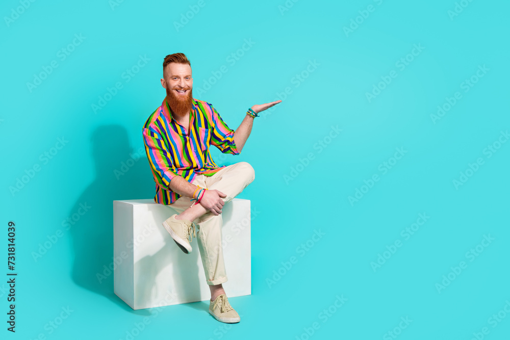 Full body length photo of bearded guy red hair businessman sit podium hold on palm new property price isolated over blue color background