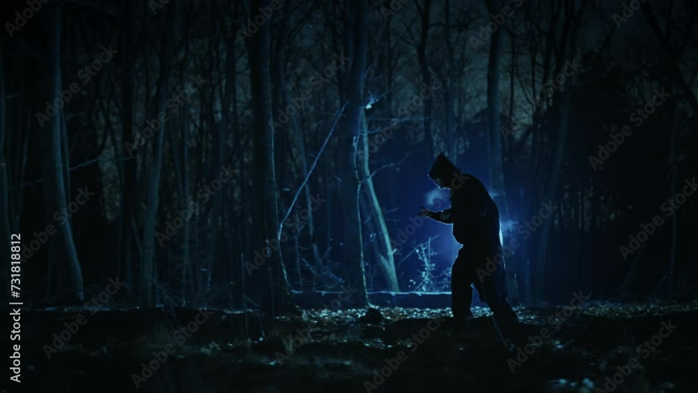 Mysterious dark figure in the night foggy forest. Silhouette of an unrecognizable man in a tunic with a hood. Mysterious dark figure in the night foggy forest. Silhouette of an unrecognizable man in a tunic with a hood.