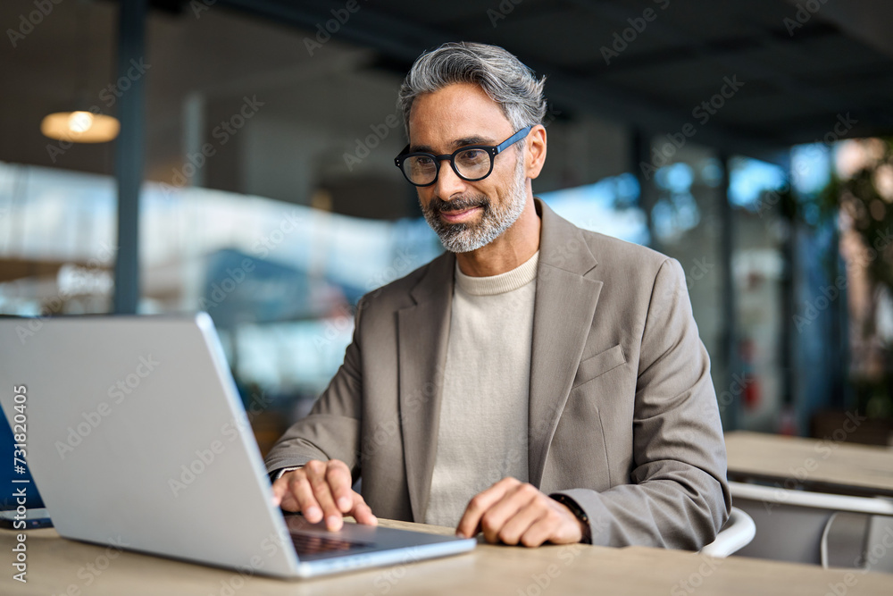 Smiling busy middle aged mature professional business man entrepreneur wearing suit and eyeglasses sitting at table outdoors working online using laptop computer hybrid working outside office. - obrazy, fototapety, plakaty 