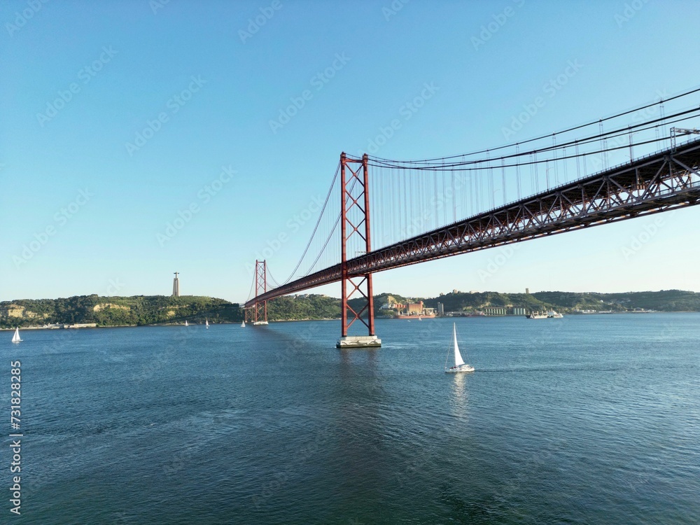 Beautiful shot of a sailboat under a bridge over Tagus River in Lisbon, Portugal