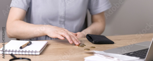 A woman counts coins poured out of her purse, cents sitting at the table. On the table is a notebook with blank sheets, a pen, a magnifying glass and a laptop. High quality photo