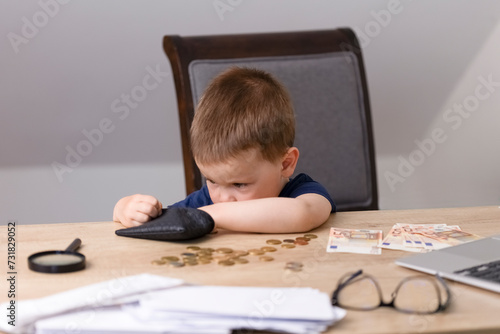 The boy pulls out money from a black wallet and counts coins. On the table next to the boy are money, a notebook, a magnifying glass, glasses and a calculator. Education and finance concept. High