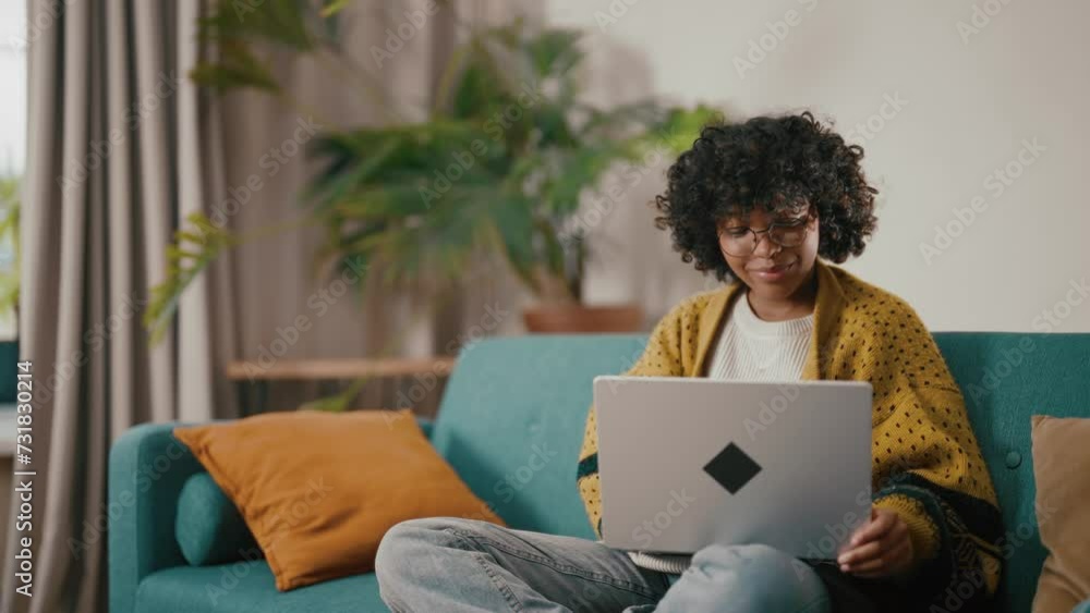 Attractive african american woman reading typing messages on laptop chatting with friends sitting at sofa at home. Smiling positive curly relaxed female enjoying online communication on computer. Attractive african american woman reading typing messages on laptop chatting with friends sitting at sofa at home. Smiling positive curly relaxed female enjoying online communication on computer.
