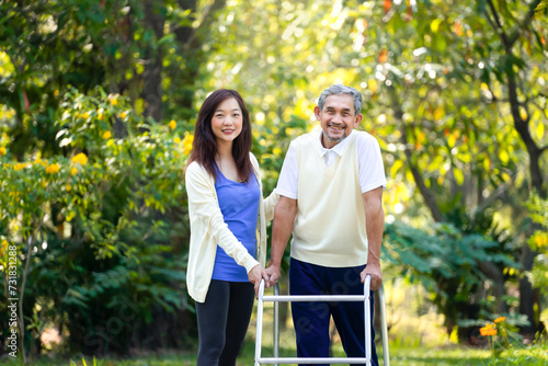 portrait young asian woman caregiver takes disability senior man practice walking with walker in the park photo