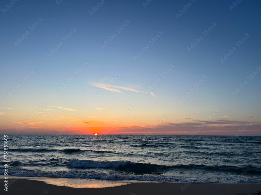 the sun rises over the water on a beach with waves