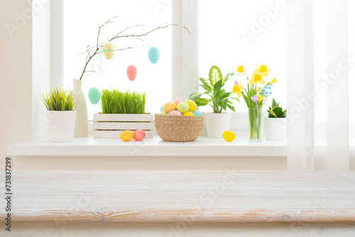 Empty easter table background in front of blurred multicolor flowers and eggs on sunny kitchen window sill photo