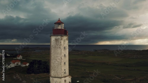 Cinematic Island lighthouse landsacape with Dark storm clouds backdrop, North sea coast. Aerial drone shot pulls in and passes the mystical tower at Kvitsøy Norway photo