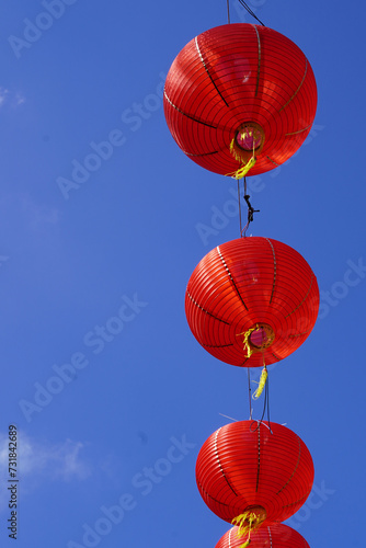A collection of red paper lanterns hanging against a clear blue sky.