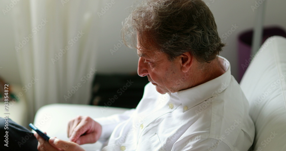Fototapeta premium Older man looking at cellphone device at home sofa