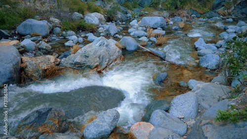 Panning mountain river at evening. Water falling down the rocks in a river. Rocky river with waterfall crystal clear water on the rocks with pebbles and sunset shadow. Wild evening river. Slow motion photo