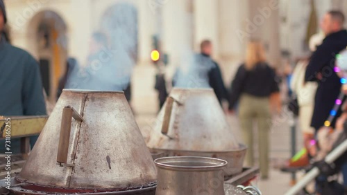 Street vendor selling roasting fresh chestnuts with smoke emitting from containers on Lisbon street. Traditional street food with blur crowd passing on Portugese city street.