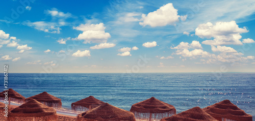 Seascape with beautiful sky and straw umbrellas on the beach on a sunny day. Horizontal banner © vvvita