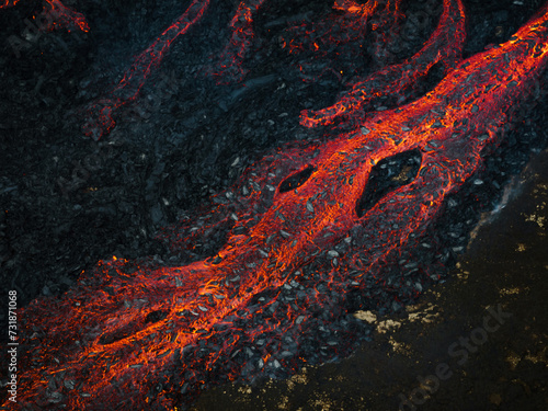 Streams of red hot lava flowing during a volcano eruption, toxic smoke covering the volcanic black field, aerial shot. Concepts of abstract patterns and backgrounds.