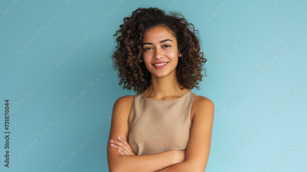 woman with curly hair is smiling at the camera, standing with her arms crossed in front of a light blue background woman with curly hair is smiling at the camera, standing with her arms crossed in front of a light blue background