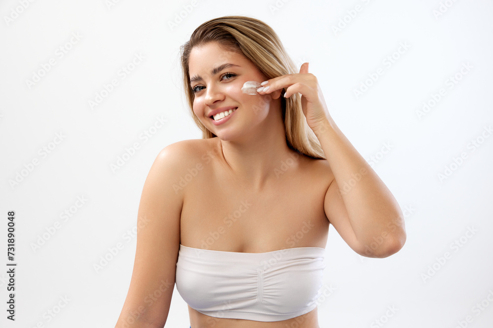 Happy woman with clear, spotless face applying cream against white studio background. Line of moisturizing creams and masks. Concept of beauty, skincare, cosmetics and cosmetology Happy woman with clear, spotless face applying cream against white studio background. Line of moisturizing creams and masks. Concept of beauty, skincare, cosmetics and cosmetology