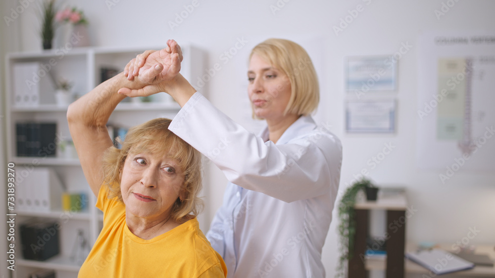 A masseur assists a senior lady with muscle stretching, providing treatment at a rehabilitation center A masseur assists a senior lady with muscle stretching, providing treatment at a rehabilitation center