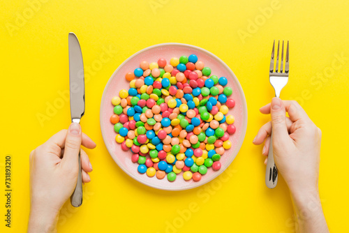 the girl holds cutlery in her hands and eats sweets in a plate. Health and obesity concept, top view on colored background