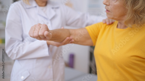 An employee at a rehabilitation center assesses a senior patient's arm following a sprain