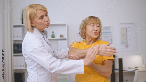 A senior woman endures difficulties while doing rehabilitation exercises with a doctor in a clinic