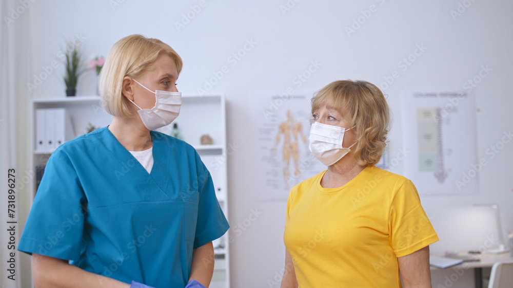 A mature female patient and doctor wearing medical masks look at each other, preparing for vaccination A mature female patient and doctor wearing medical masks look at each other, preparing for vaccination