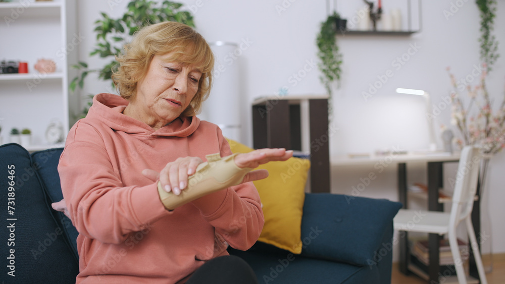 A senior woman examines her injured hand wrapped in a medical band, contemplating a new treatment A senior woman examines her injured hand wrapped in a medical band, contemplating a new treatment