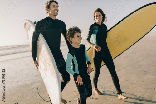 Family in wetsuits carrying boards on the beach photo