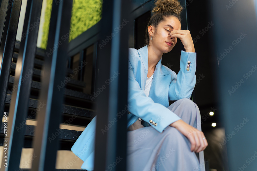 In the grip of job-related stress and exhaustion, she rests on the staircase that leads to her office.