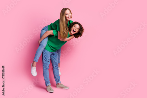 Full body photo funky laughing couple riding girl piggyback joking together looking empty space at party isolated on pink color background