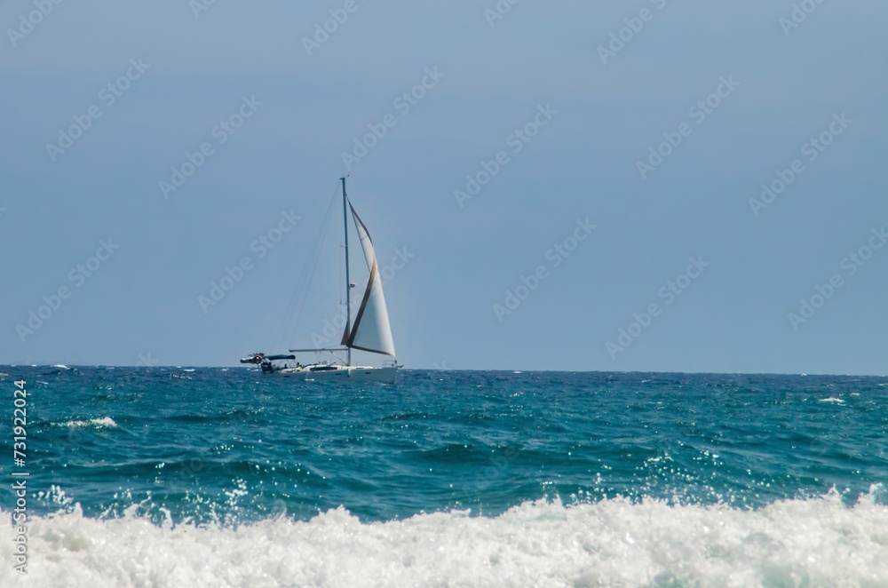 Naklejka premium Velero navegando en el horizonte en cabo de Gata, España. Yate a toda vela navegando en las aguas turquesas del Mar Mediterráneo.