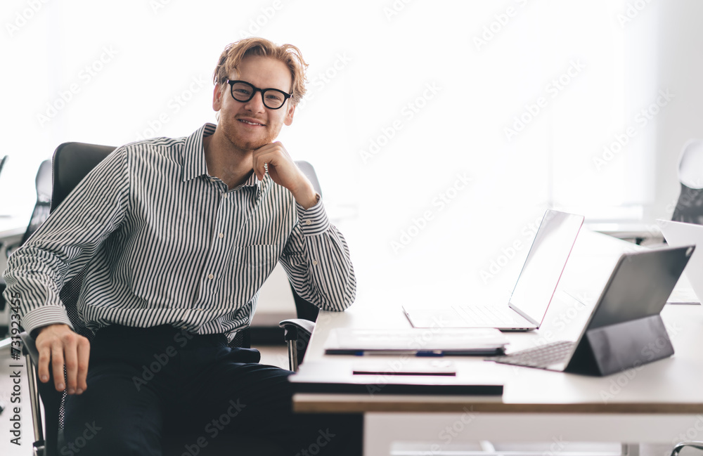 Smiling man sitting at office desk with hand at chin Smiling man sitting at office desk with hand at chin