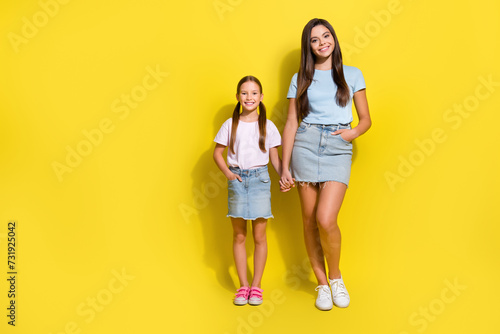 Full length photo of pretty good mood small siblings dressed t-shirts holding hands arms empty space isolated yellow color background photo