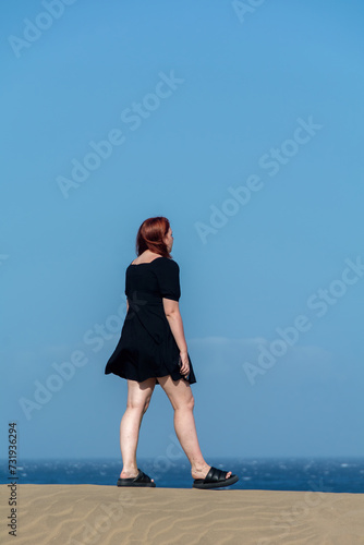 Young woman in a black short  dress stands on a sand dune © Claudia Evans 