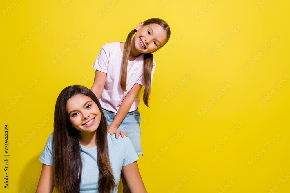 Photo of pretty sweet little sisters wear t-shirts having fun empty space isolated yellow color background Photo of pretty sweet little sisters wear t-shirts having fun empty space isolated yellow color background