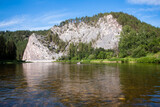 Tranquil River Scene with Rocky Cliff, Lush Green Trees, and Serene Blue Sky