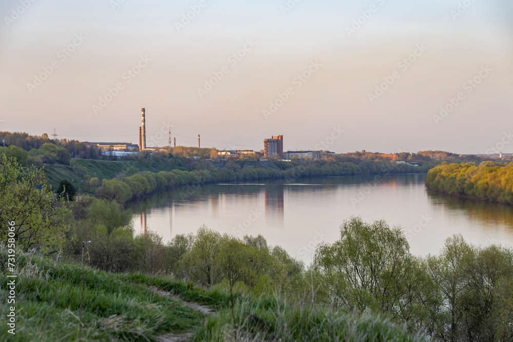View of factory chimneys near a wide river, autumn landscape