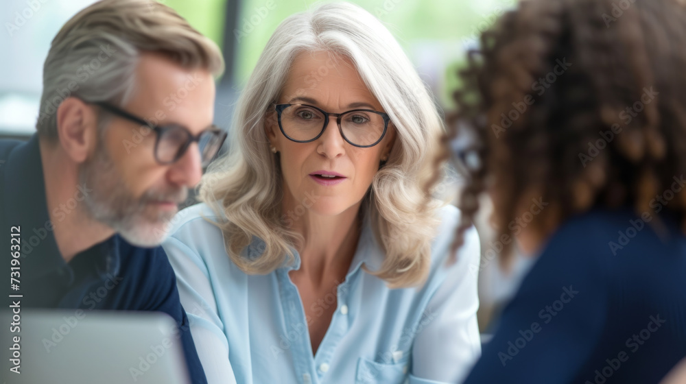 A professional with glasses is intently discussing with colleagues, one with a laptop, in a collaborative office setting, conveying mentorship and leadership. A professional with glasses is intently discussing with colleagues, one with a laptop, in a collaborative office setting, conveying mentorship and leadership.